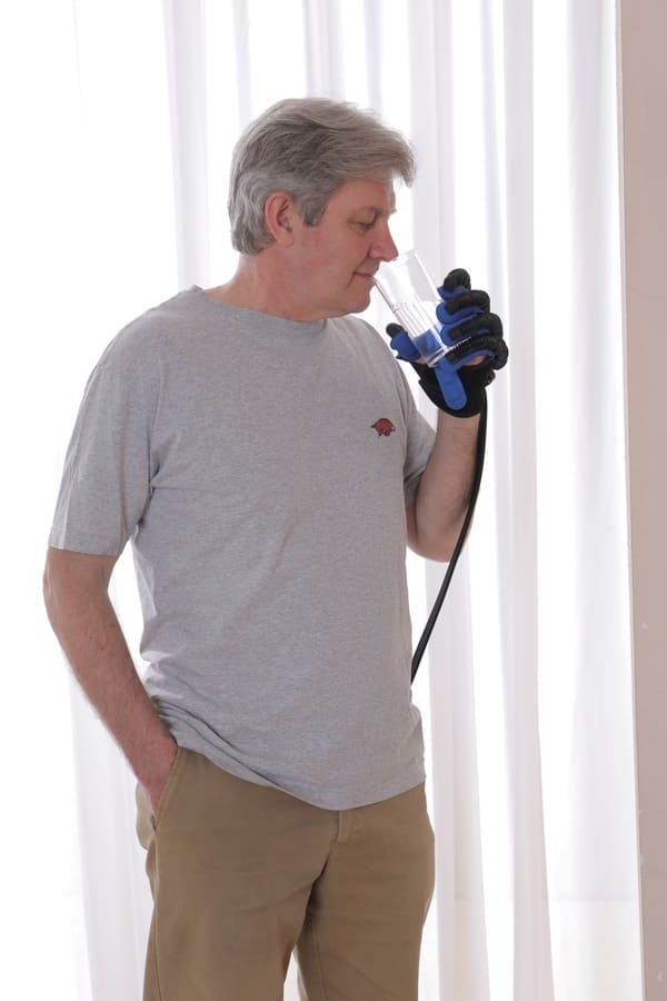 Patient at home drinking from a glass while wearing the Syrebo C12 power glove